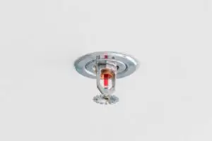A fire sprinkler head mounted on a white ceiling, ready to activate in case of fire.