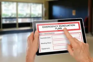 Person holding a tablet displaying a home fire escape plan with sections for general guidelines, available exits, meeting place, and equipment.
